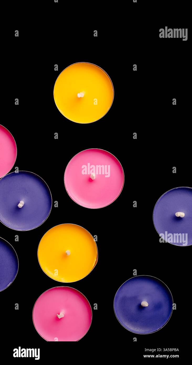 Tea lights in pink, yellow, and blue, top view composition against a black backdrop. Stock Photo