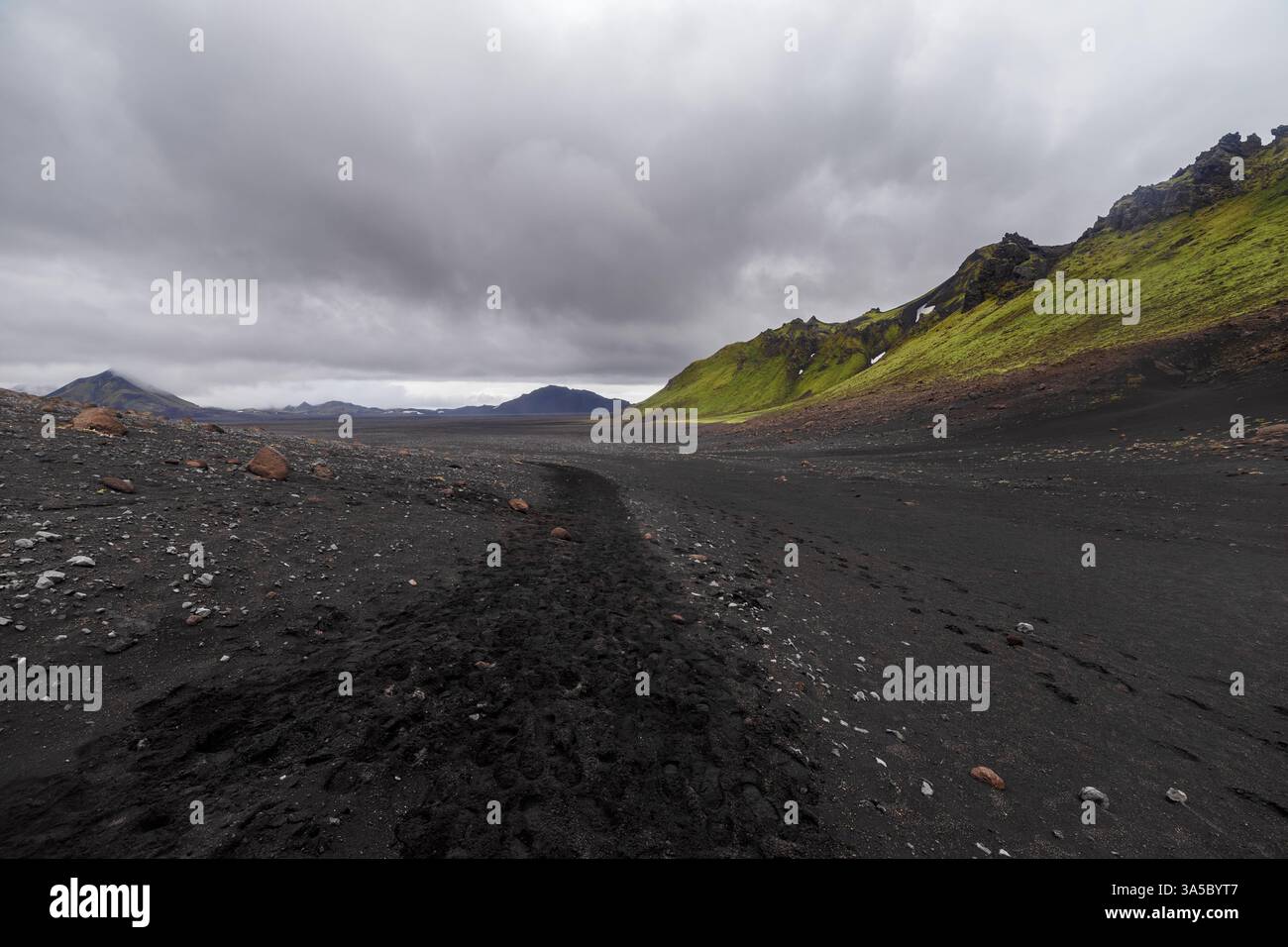 Stunning Landscape of Volcanic Terrain with Green Hills and Dark Ash Ground Under a Dramatic Cloudy Sky in Iceland s Unique Natural Beauty Stock Photo