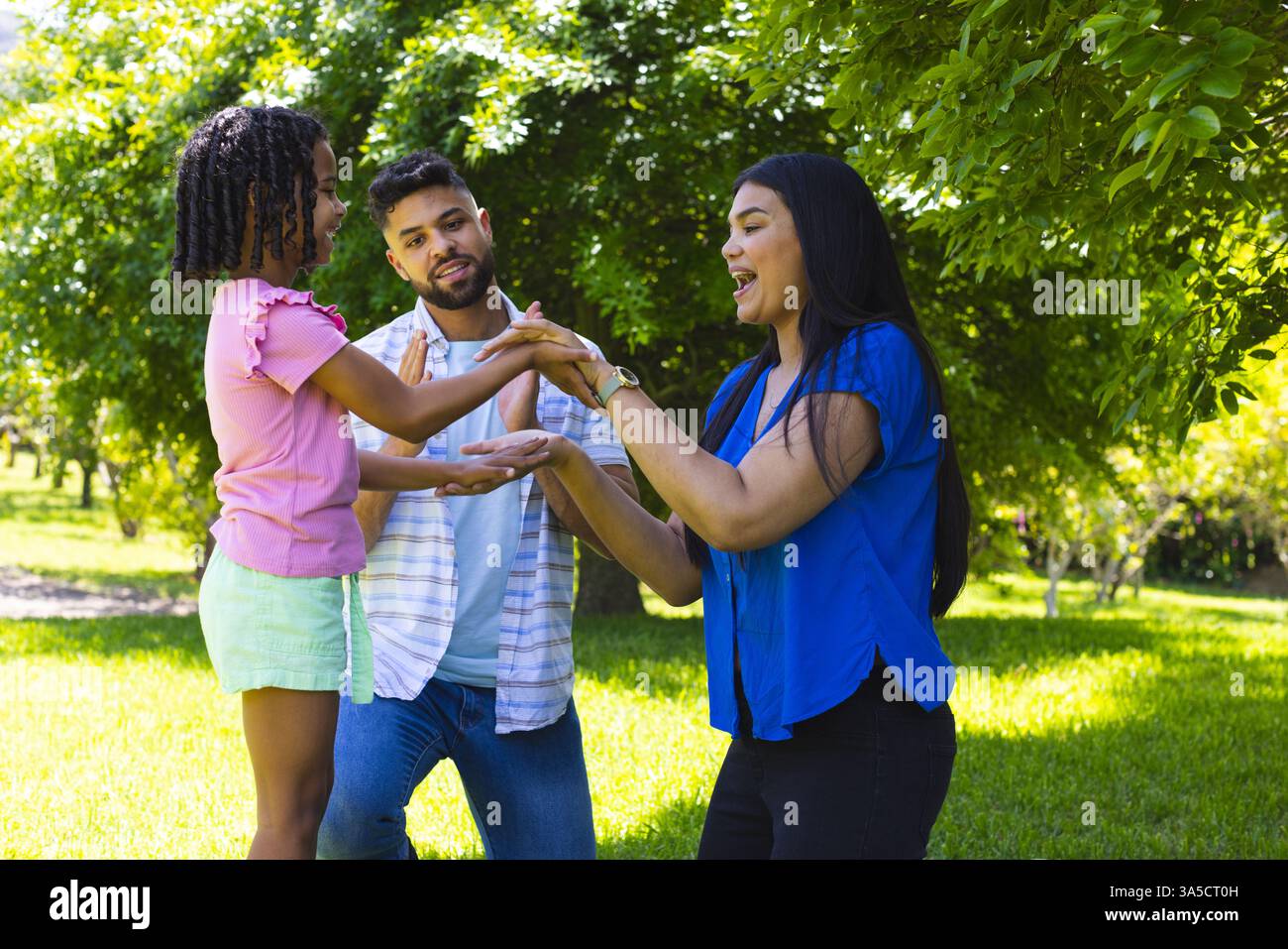 Family enjoying playful moment outdoors, smiling and bonding under sunny trees Stock Photo