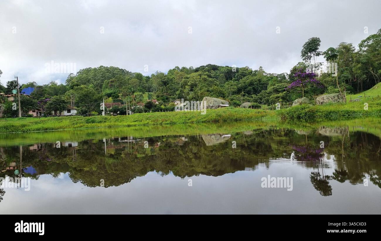 A serene rural valley stretches between lush green hills, where scattered houses rest quietly among trees and grassy fields. - Smartphone Captured Stock Image