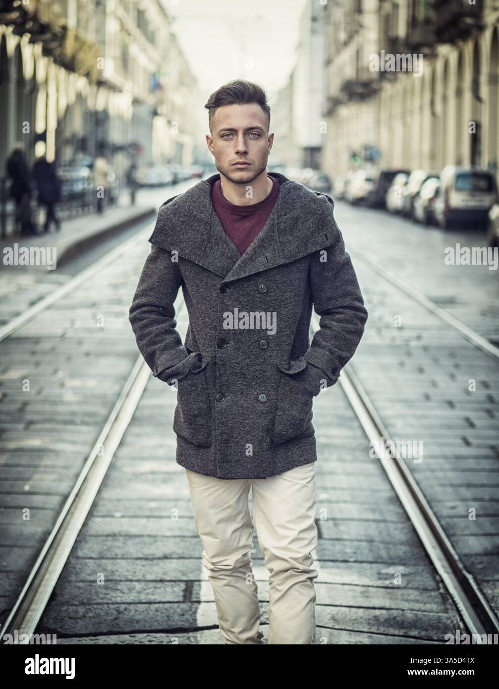 Attractive young man standing in the middle of city street looking at ...