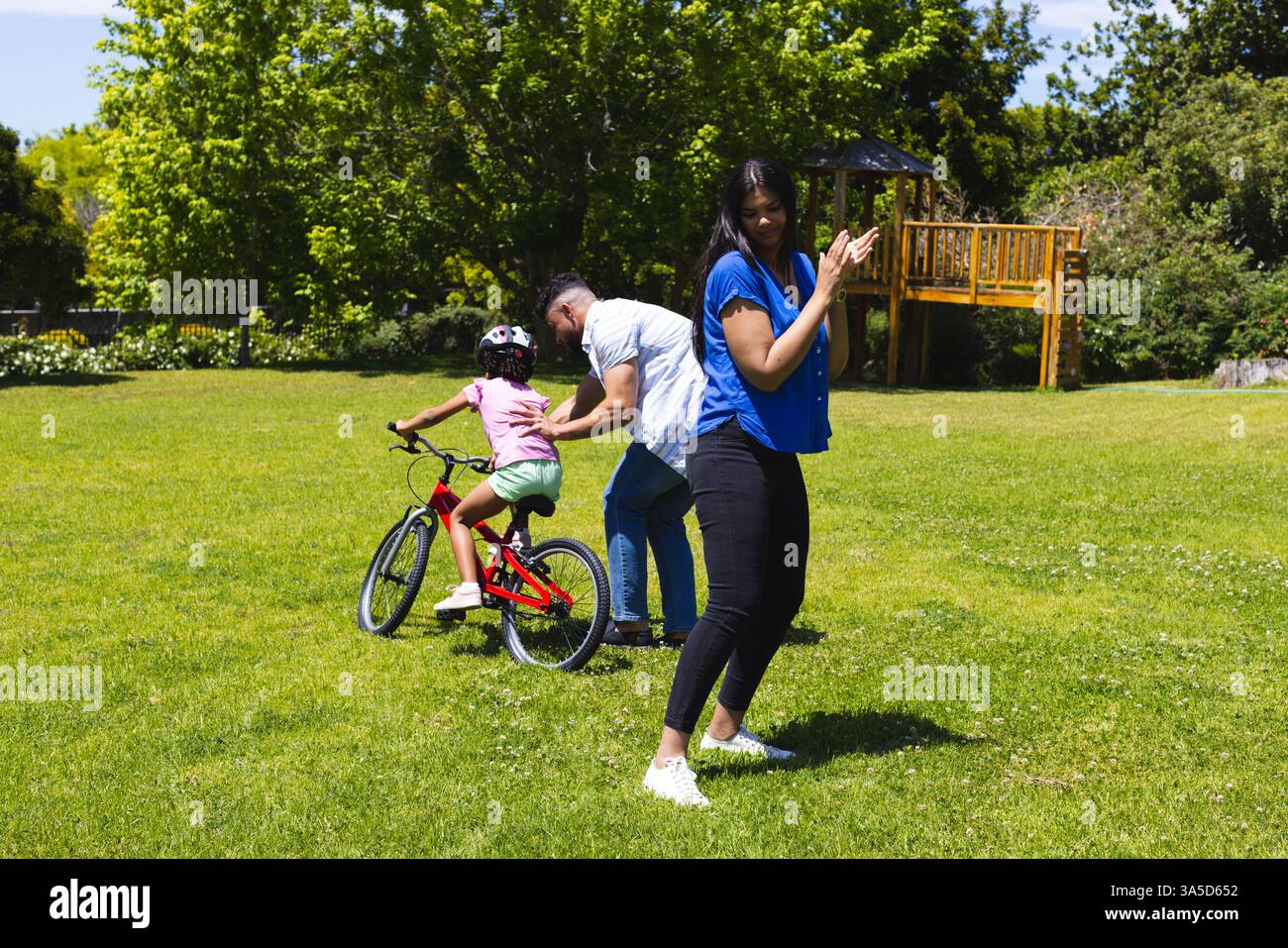 Child Rode Save Father helping child ride bicycle in park while mother clapping and ...