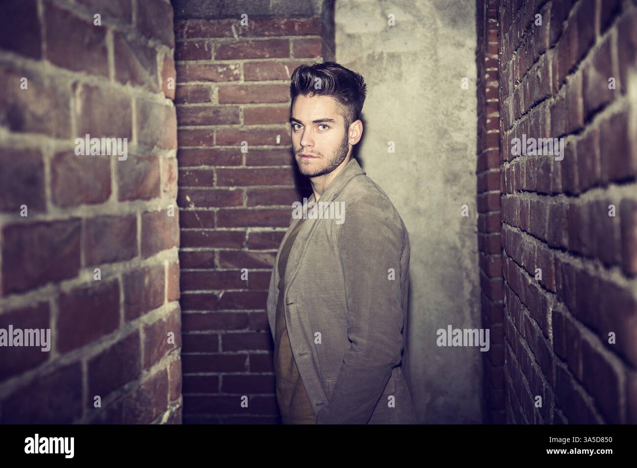 Attractive young man standing against brick wall, looking at camera Stock Photo