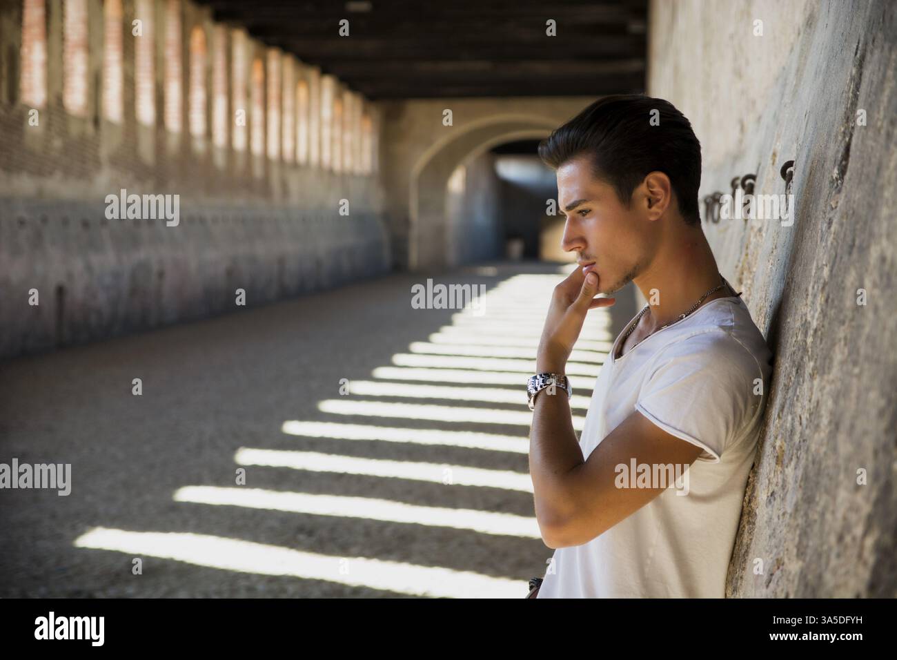Handsome young man in old building against brick wall, looking down Stock Photo