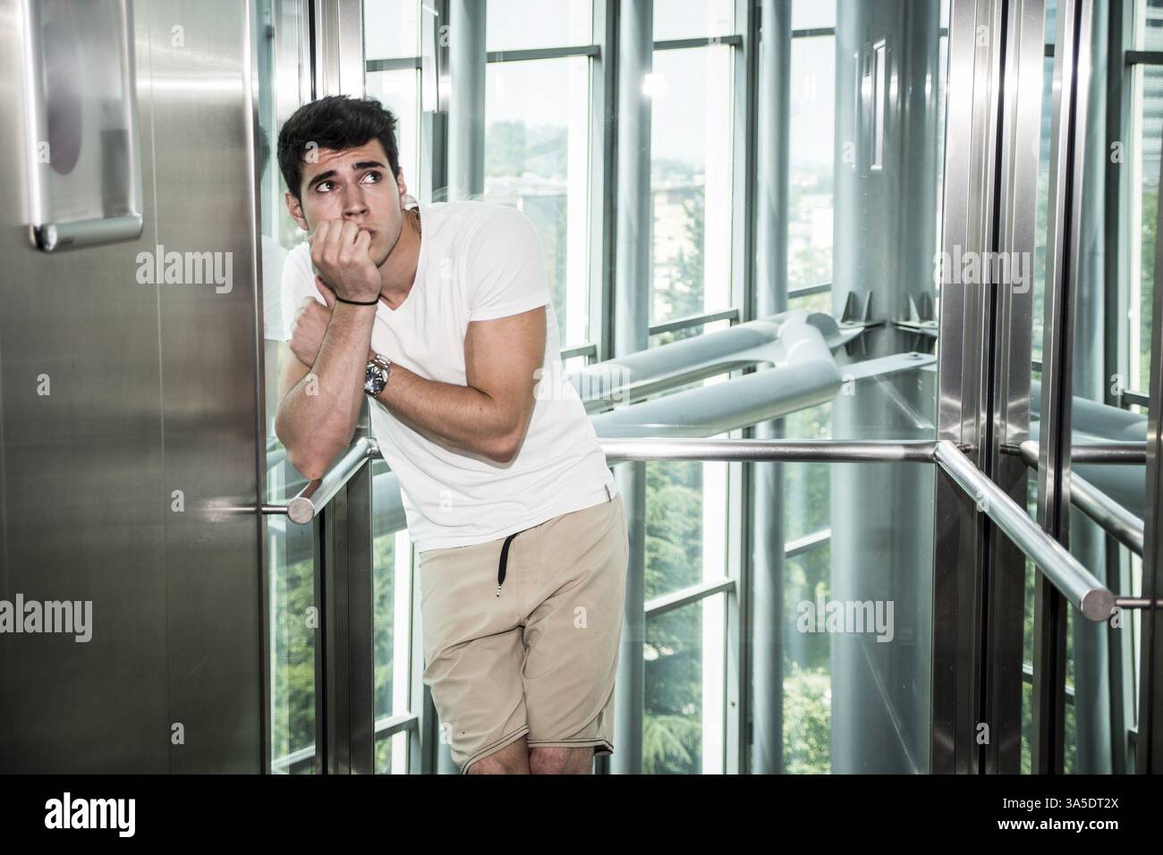 Scared young man desperate in stuck elevator screaming, looking very upset Stock Photo