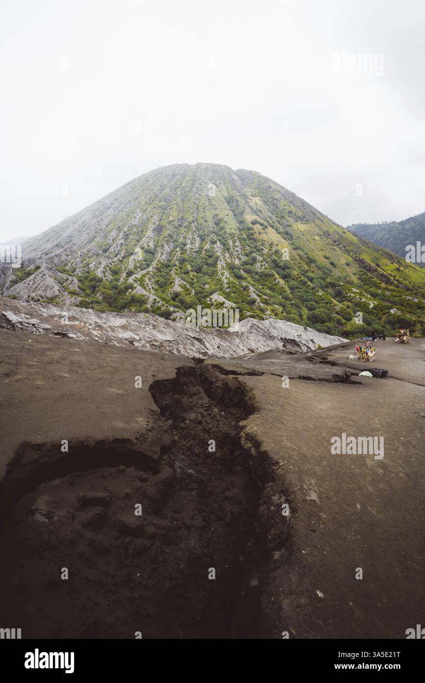 Green volcanic mountain towers above, people explore the barren and rugged landscape, Bromo volcano, Sri Lanka, Asia Stock Photo