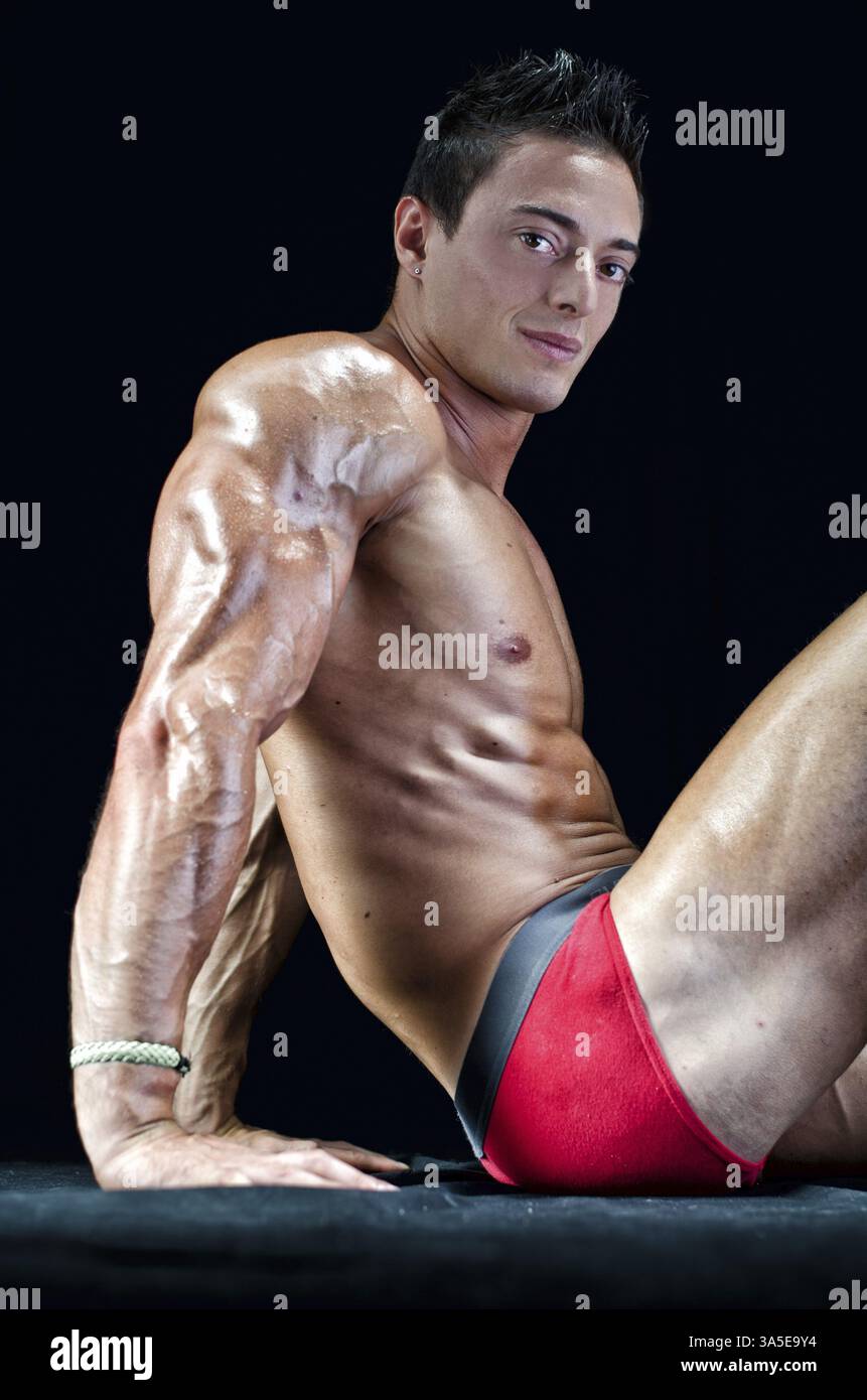 Handsome young man with muscular body, sitting on the floor showing ripped tricep, arm and abs Stock Photo
