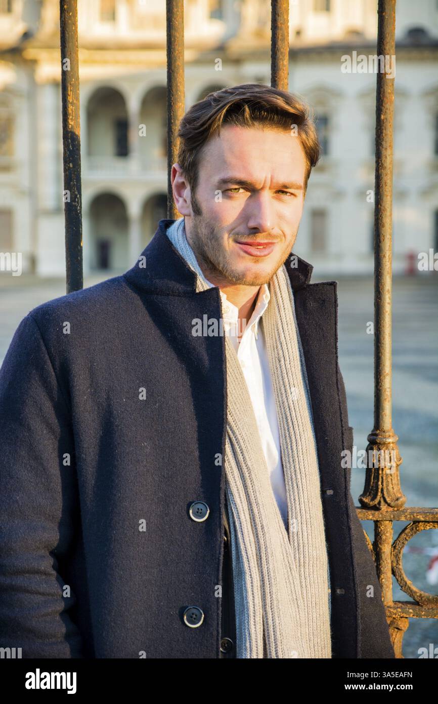 Waist Up of Stylish Young Man Wearing Coat and Looking Up in front of Historical Building in Background Stock Photo
