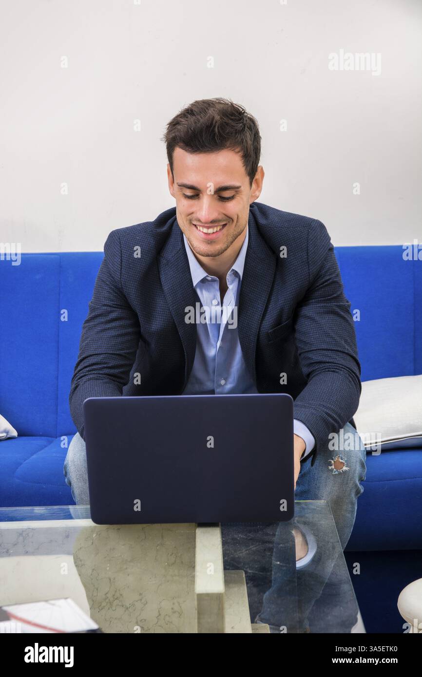 Attractive young man using laptop PC while laying on couch, with happy expression Stock Photo