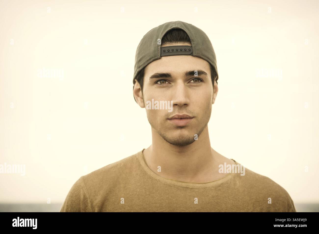 Portrait of handsome young man outside wearing baseball cap, looking at camera. Head and shoulders shot Stock Photo