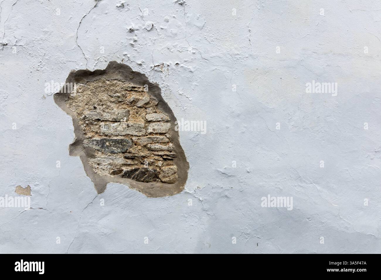 Front view white plastered wall with damaged part, original stones visible for​ vintage​ background. Stock Photo