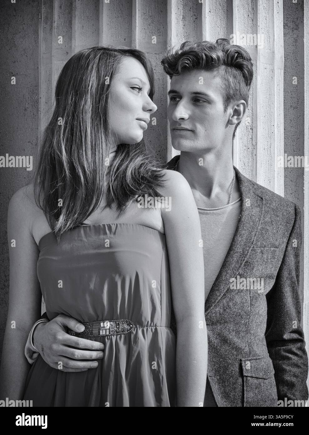 Elegant young couple standing in front of old stone column looking at ...