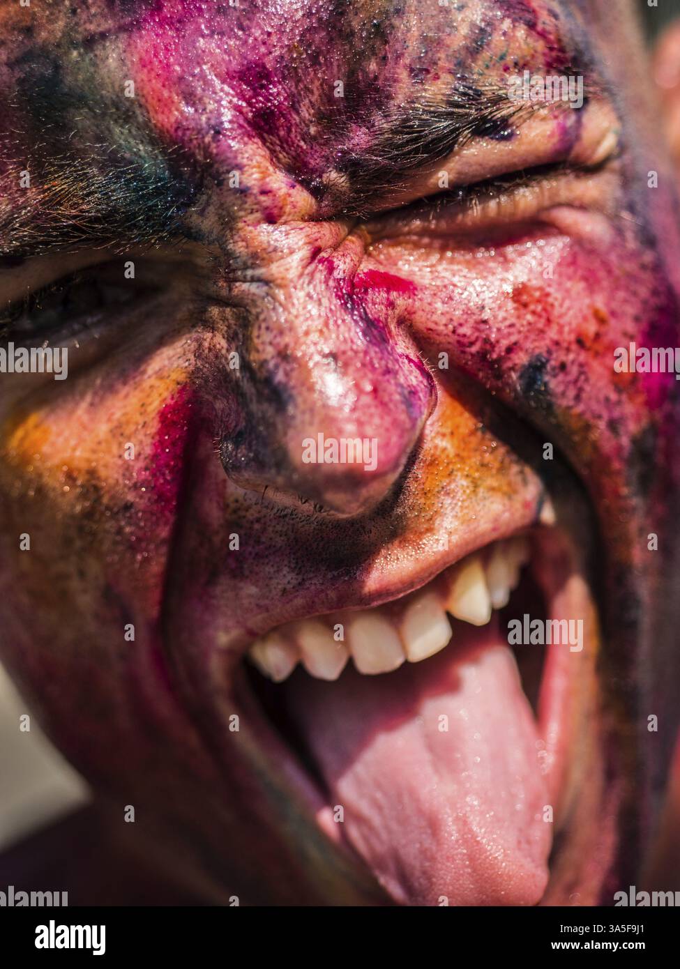 A close up of a painted man with his mouth open, doing silly face with tongue sticking out and one eye winking Stock Photo
