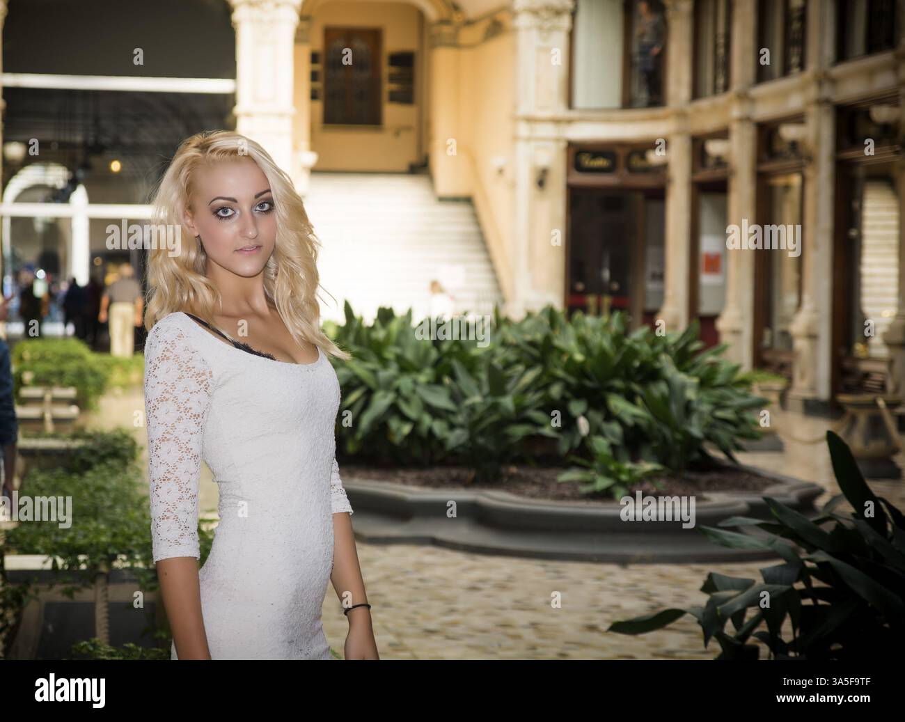 Elegant pretty blonde young woman standing in white dress in posh city setting in Europe Stock Photo