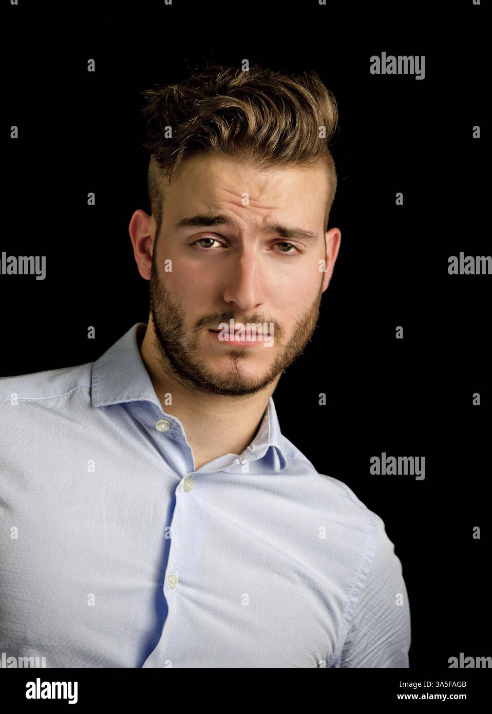 Handsome young man portrait with doubtful, unsure expression, isolated on black background Stock Photo