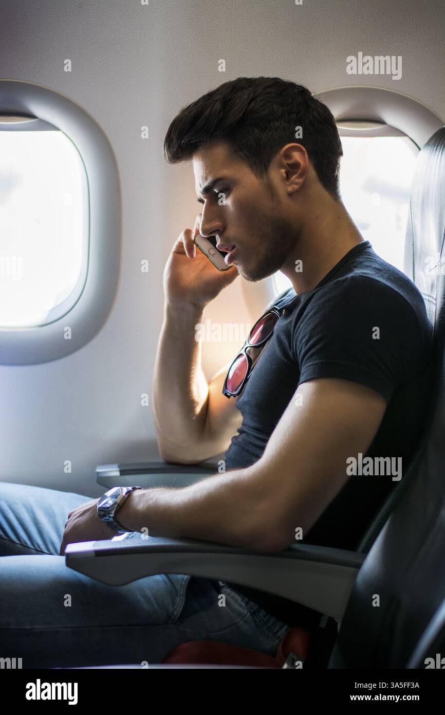 Side view of handsome young man against plane window sitting and talking on the phone Stock Photo