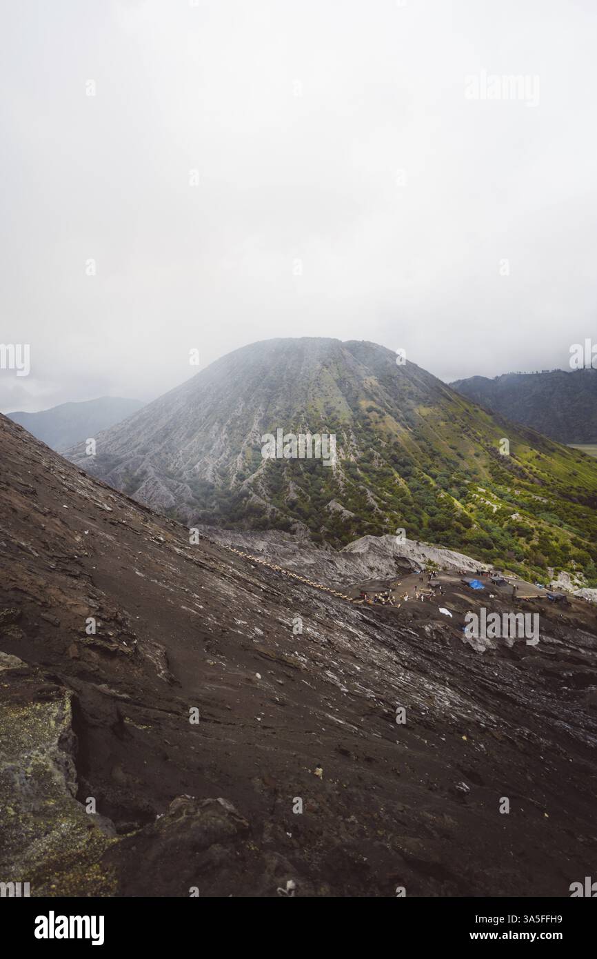 Green volcanic mountain rises above a barren landscape under a misty sky, Bromo Volcano, Sri Lanka, Asia Stock Photo