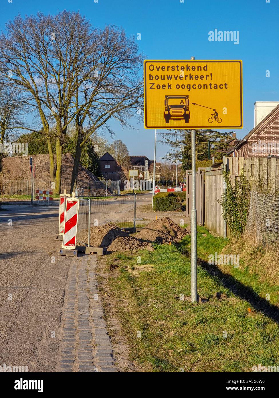 Yellow traffic sign w/ icon of truck & cyclist; warning that looking for eye contact w/ crossing construction traffic is advisable for safety reasons - Smartphone Captured Stock Image
