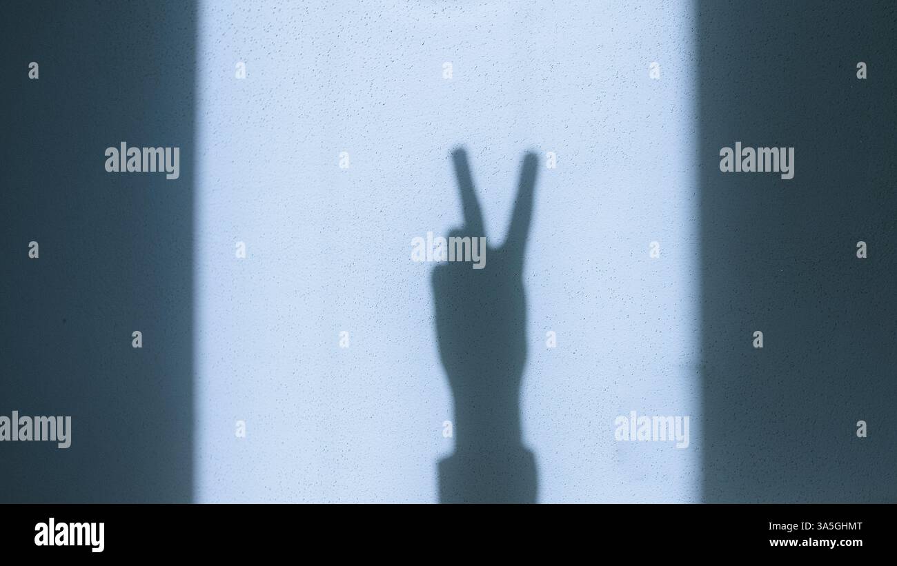 Shadow of a hand making the peace sign on a sunlit wall, symbolizing ...