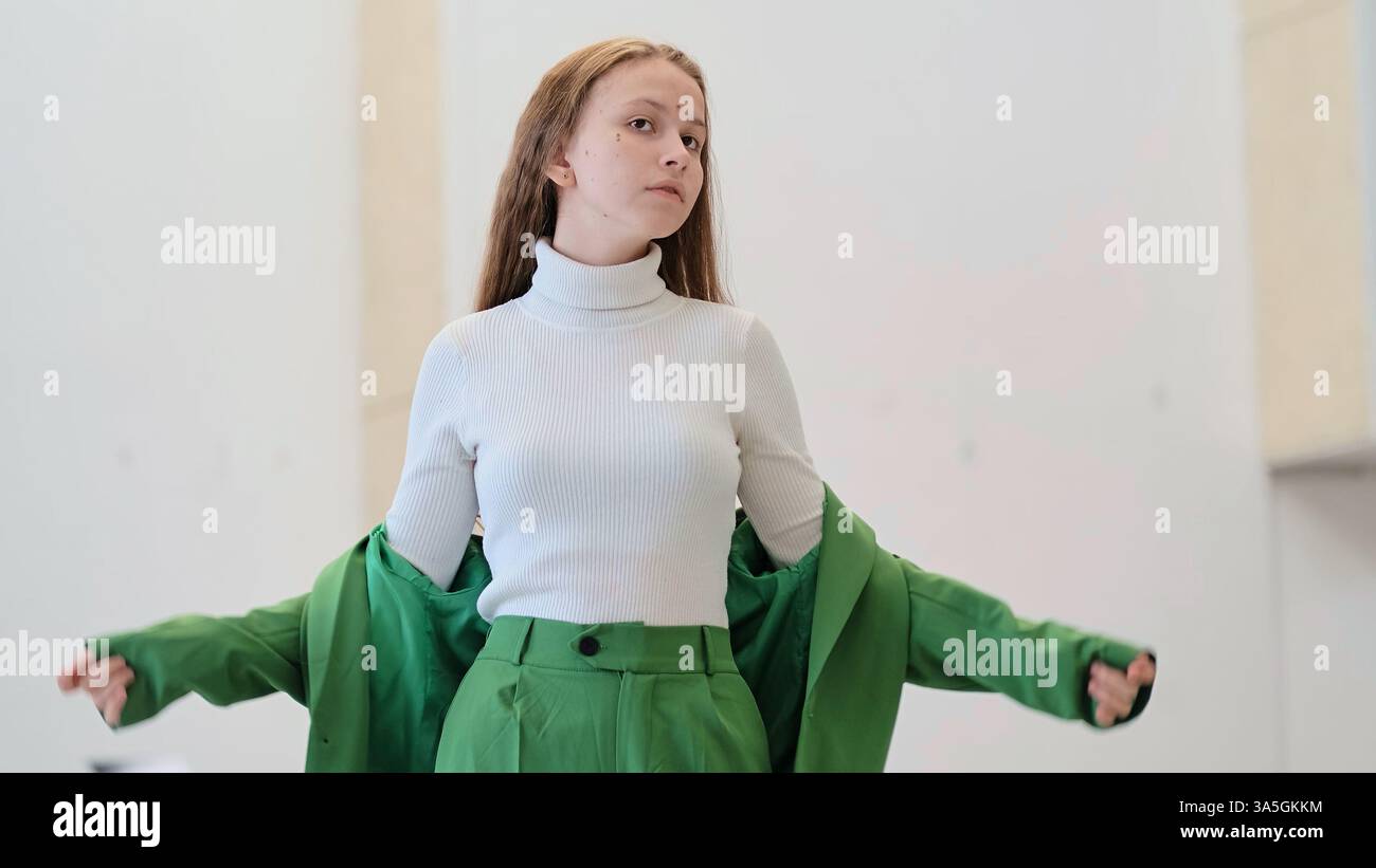 A young woman confidently removes her green jacket, wearing a white ...