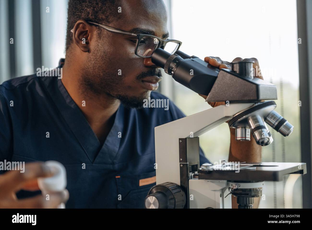 Test tube in hand, using the microscope. Scientist is working indoors. Stock Photo