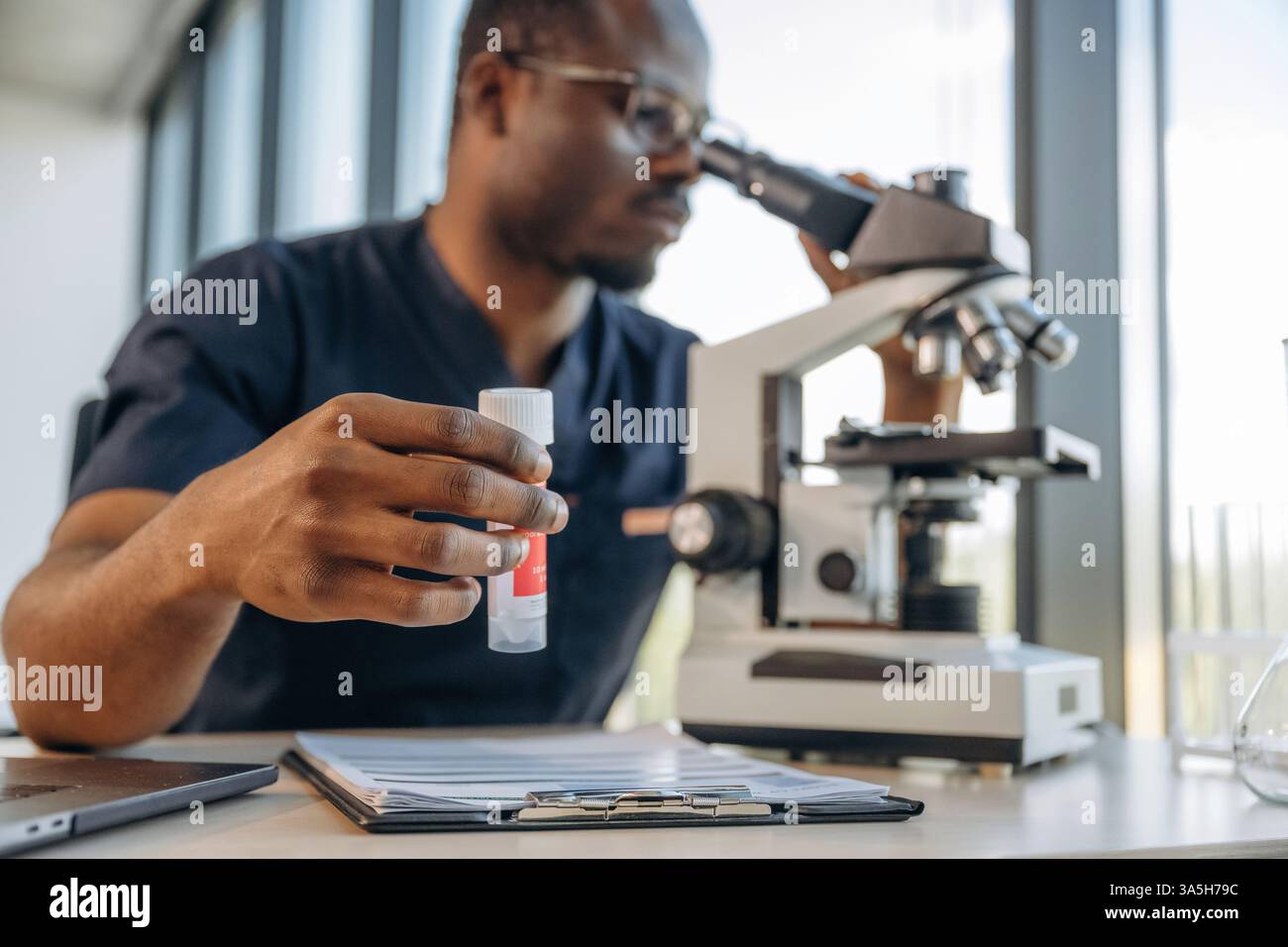 Test tube in hand, using the microscope. Scientist is working indoors. Stock Photo