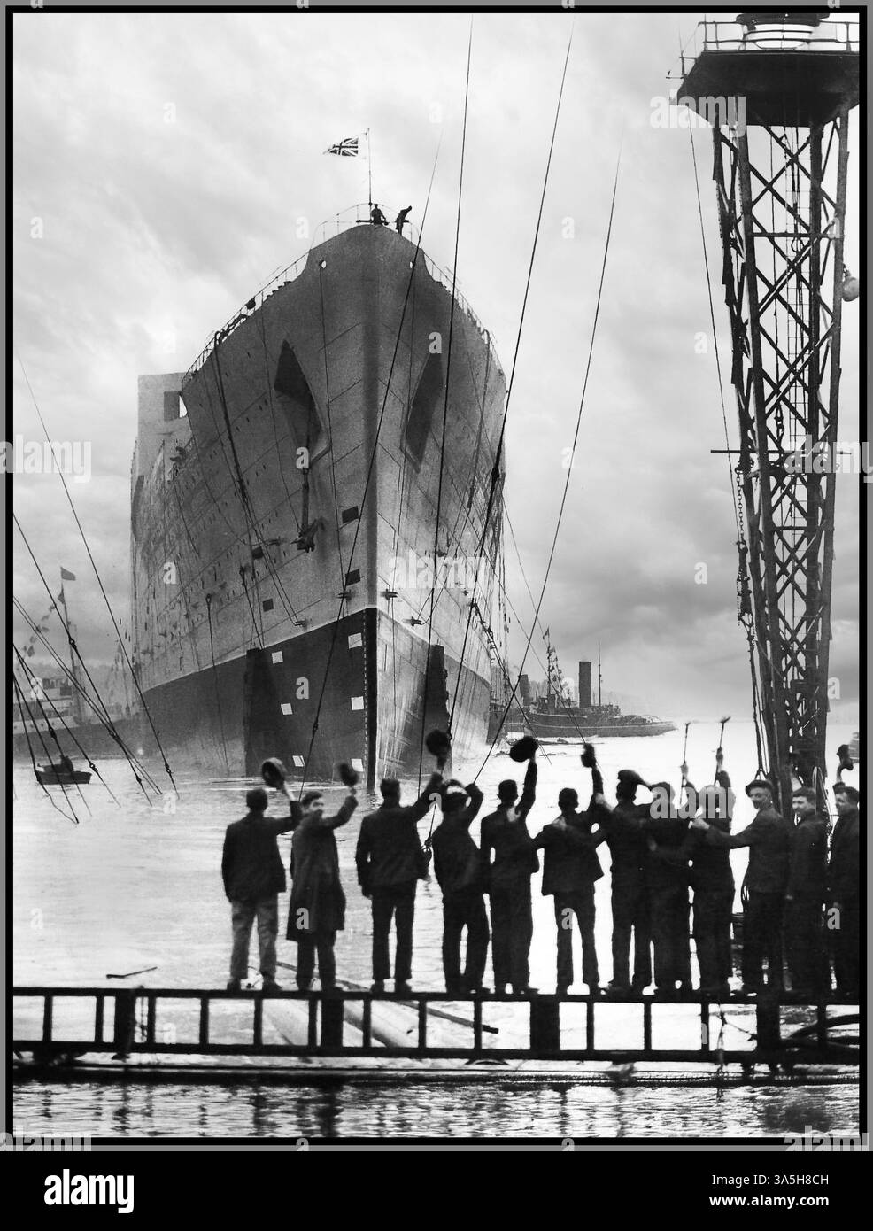QUEEN MARY OCEAN LINER LAUNCH LAUNCHING SLIPWAY 1934 Cunard White Star Line launched RMS Queen Mary. Shipworkers in foreground wave her off.  The construction of the ship, then known only as 'Hull Number 534,' began in December 1930 on the River Clyde, Scotland, by the John Brown & Company shipyard at Clydebank. Photographs of RMS Queen Mary on the River Clyde, showed the ship with no funnels, and historic records show that the “fitting out” of the interiors were still to be done. The ship was finally completed in 1936 and was ready for her maiden voyage to New York at the end of May 1936. Stock Photo