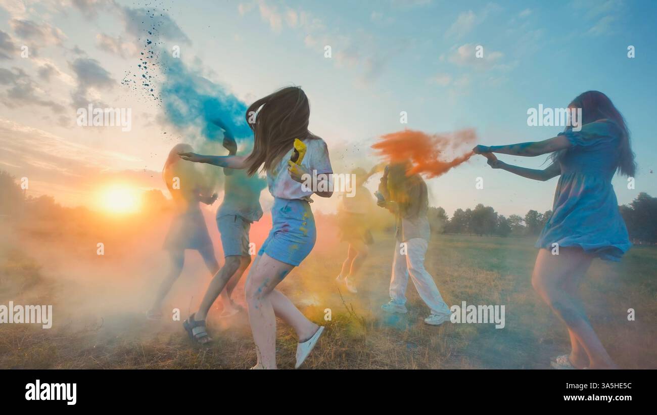 Young group joyfully throwing colored powder at sunset, celebrating the ...