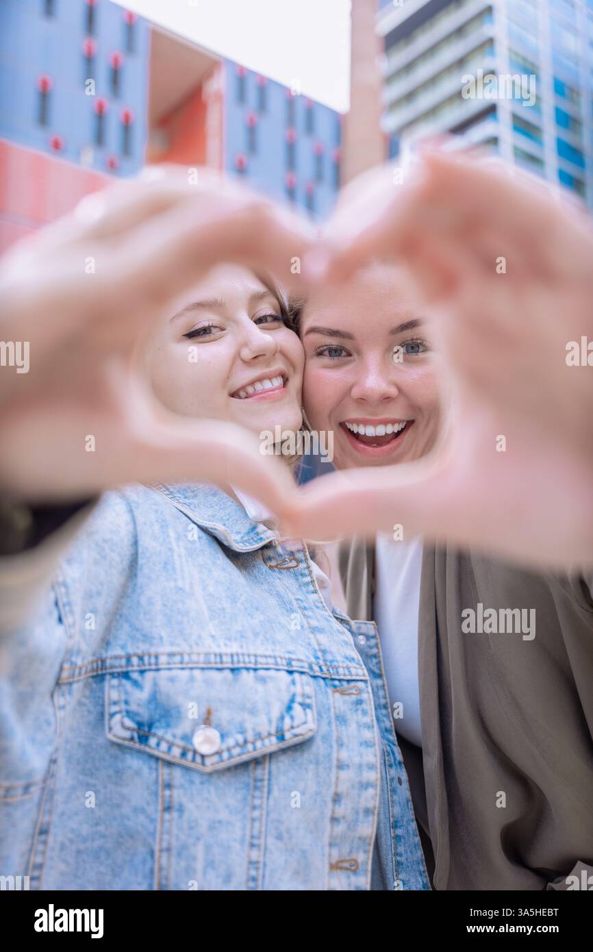 Happy Caucasian friends making a heart shape with hands and smiling outdoors Stock Photo