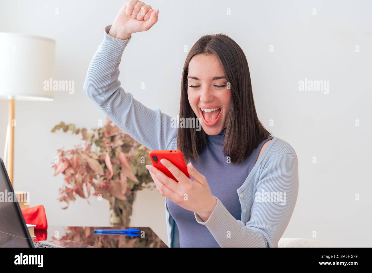 Excited Caucasian woman looking at smartphone while sitting at home office desk Stock Photo