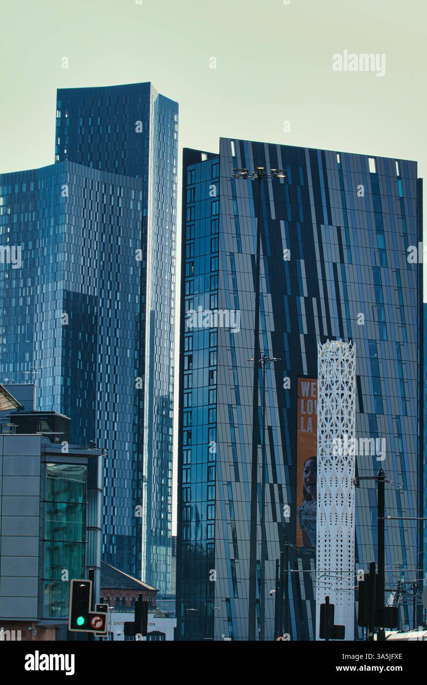 The image shows multiple modern, blue-toned skyscrapers and an ornamental tower in an urban setting, under a pale sky in Manchester, UK. Stock Photo