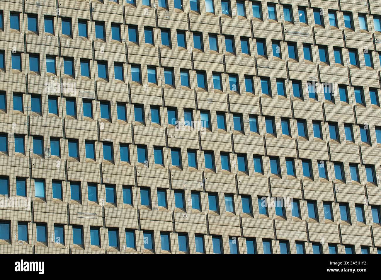 Close-up of a building's facade with many identical windows in a regular grid pattern. The building's material is light brown in Manchester, UK. Stock Photo