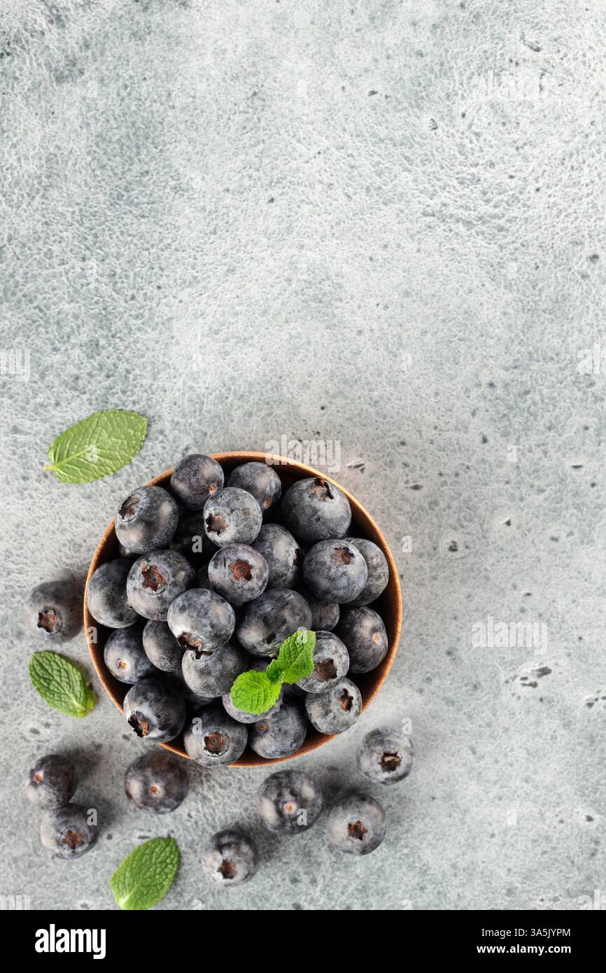 Wooden bowl of fresh blueberries with green mint leaves on blue background. Top view. Copy space Stock Photo