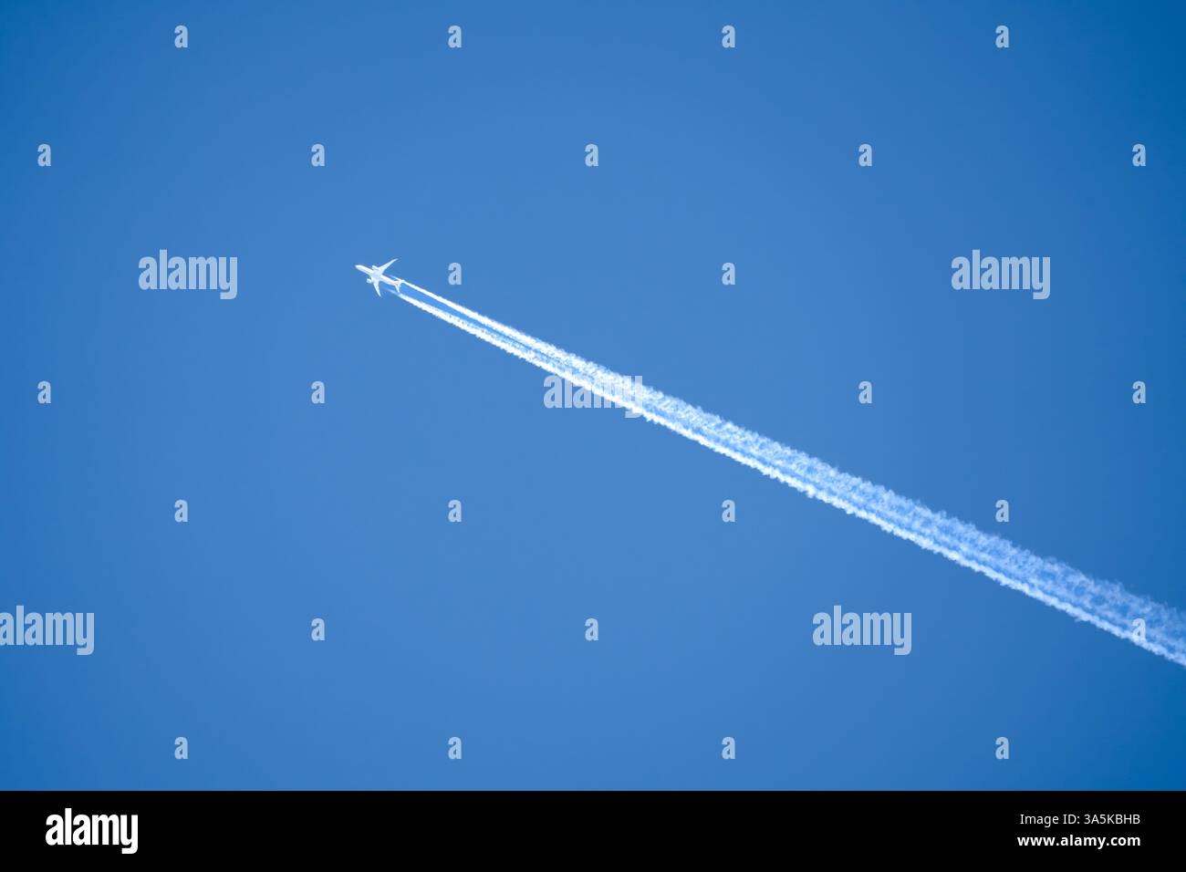 a twin engined jet liner aircraft in deep blue sky, contrails vapour ...