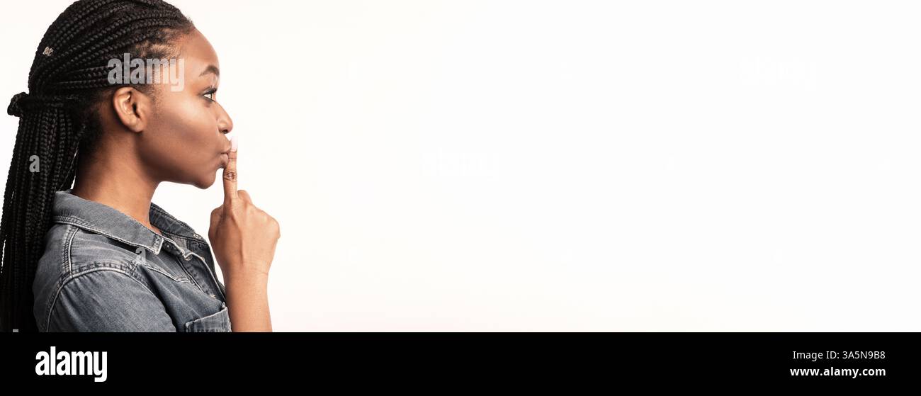 A woman with braided hair gestures for silence in a bright studio setting Stock Photo