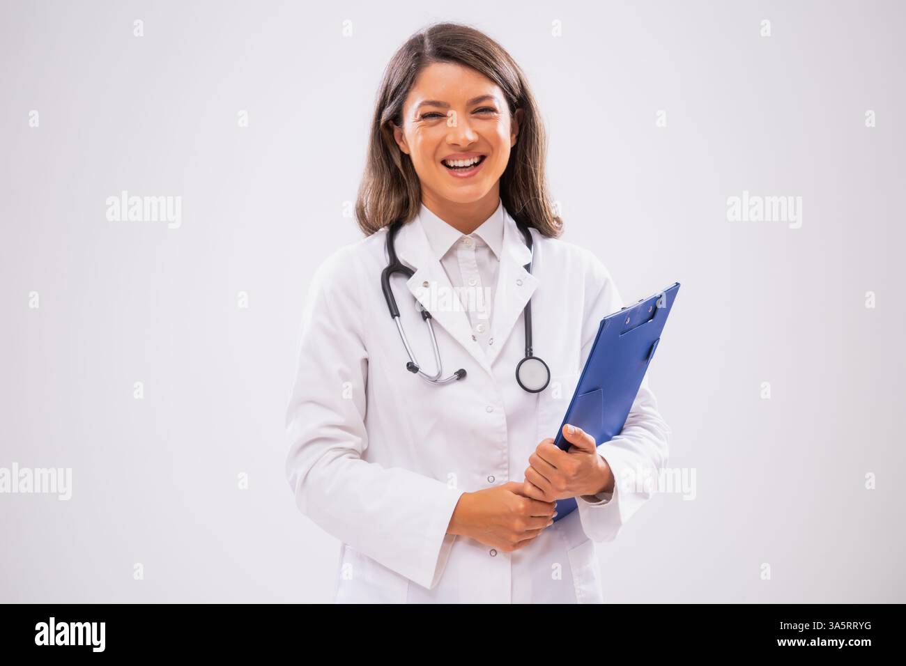 Studio shot portrait of cheerful female doctor who is holding clipboard and smiling. Stock Photo