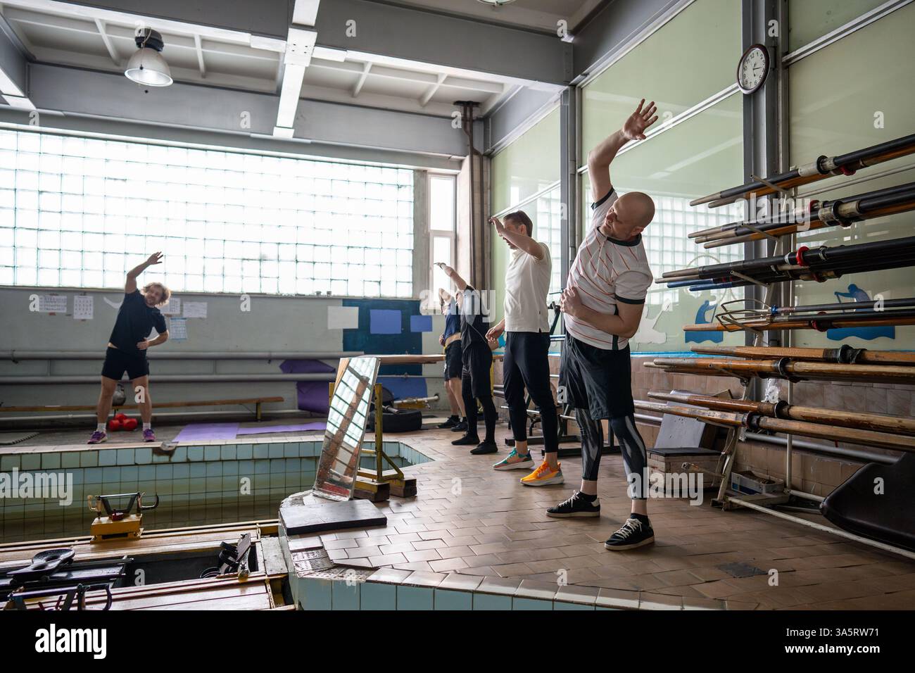 Determined concentrated athlets execute side bend under coach guidance, preparing for rowing workout Stock Photo