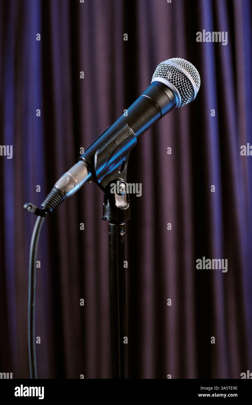Microphone standing on stage with dark blue curtain in the background, ready for performance, presenting an artistic ambiance for music or speeches Stock Photo