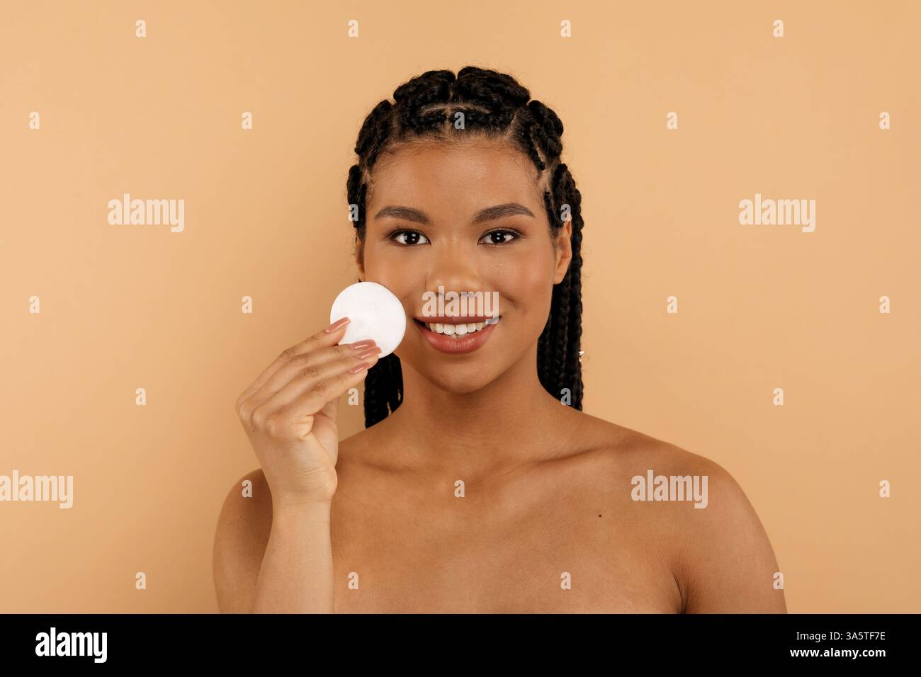 Young woman smiling while holding cotton pad, cleansing skin Stock Photo