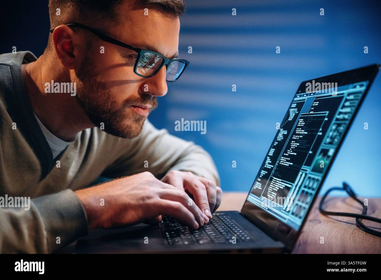 Side view. Male programmer is working indoors by a laptop. Stock Photo