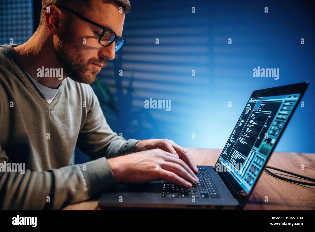 Side view. Male programmer is working indoors by a laptop. Stock Photo