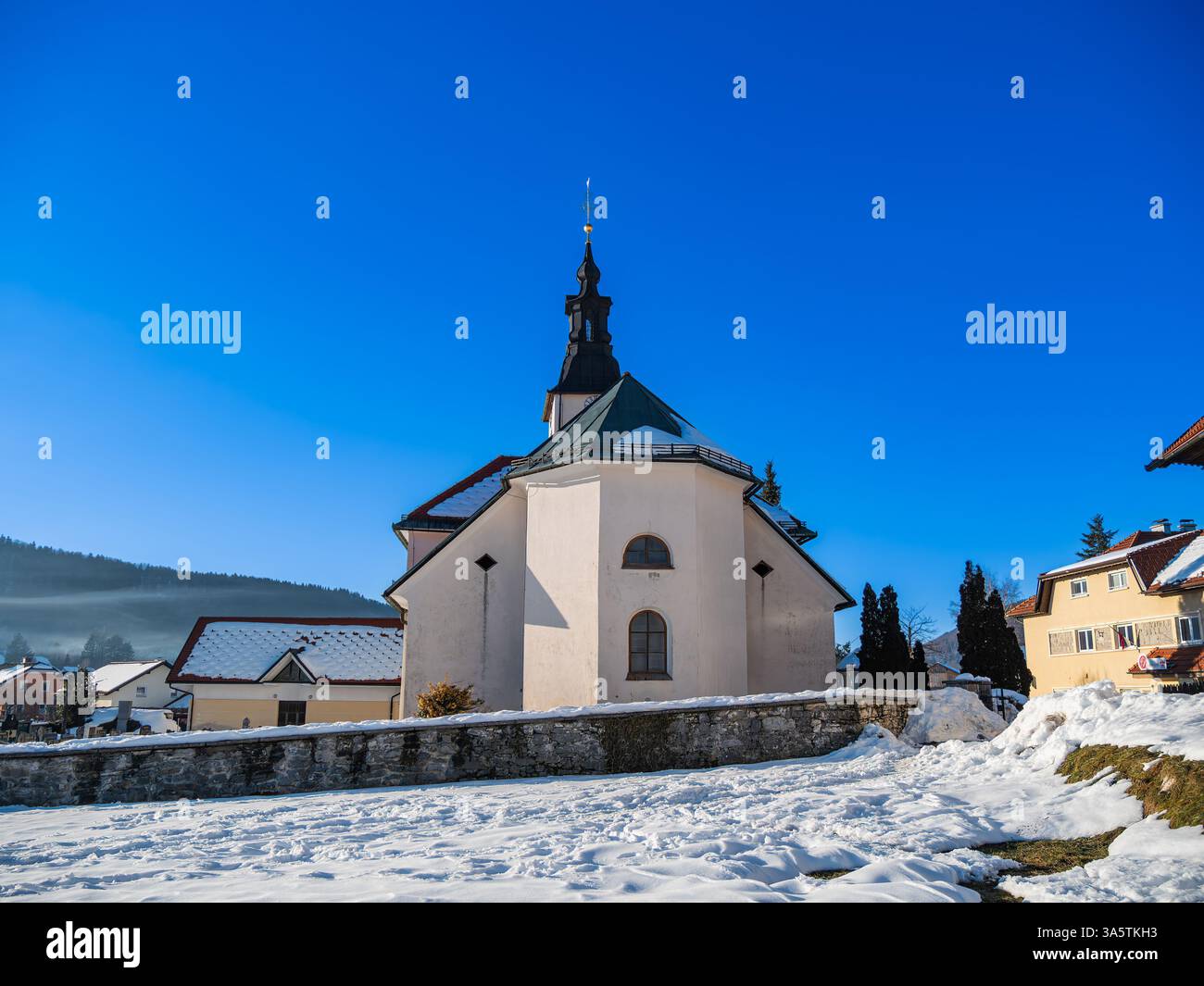 A picturesque church surrounded by snow-covered ground under a clear blue sky. The building features a distinctive steeple and is set against a backdr Stock Photo
