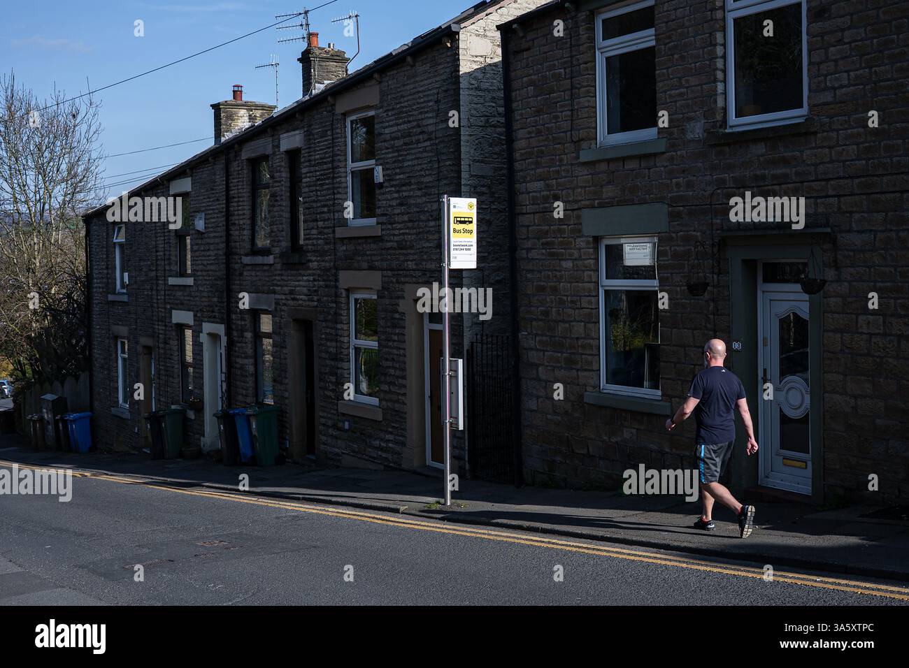 A man walks past a ‘Bee Network’ Bus Stop in the town of Mossley, Greater Manchester, UK. Stock Photo
