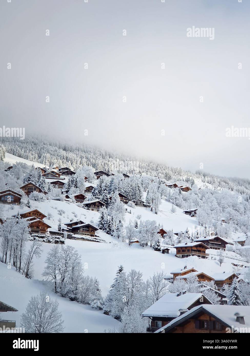 Idyllic winter scene of snow covered La Clusaz village nestled in a hilly landscape, Annecy, France. Wooden houses are scattered across the snowy hill - Smartphone Captured Stock Image