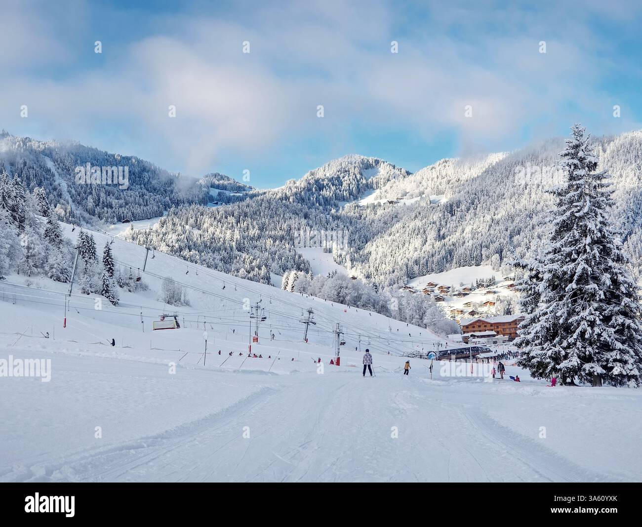 Picturesque snowy mountain landscape with slopes, lifts, and skiers at La Clusaz ski resort, Annecy, France. Snow covered woods and a small village wi - Smartphone Captured Stock Image