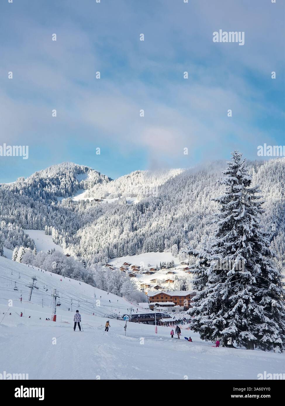 Mountain ski resort landscape with slopes, lifts, and skiers at La Clusaz, Annecy, France. Snow covered woods and a small village with cabins nestled - Smartphone Captured Stock Image