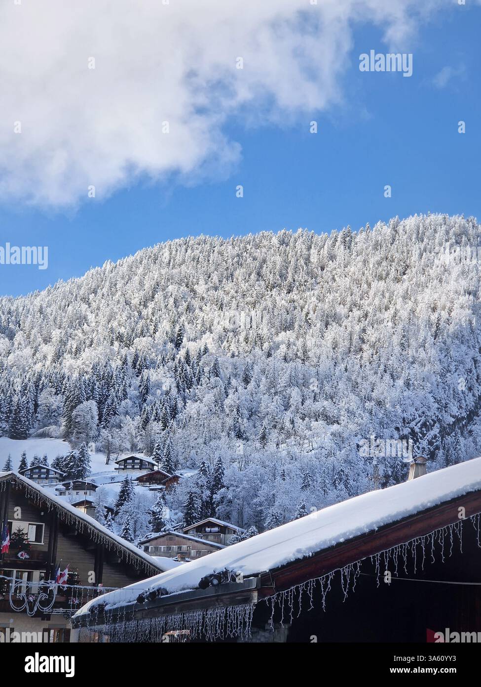 Idyllic winter scene of snow covered La Clusaz village nestled in a hilly landscape, Annecy, France. Wooden houses are scattered across the snowy hill - Smartphone Captured Stock Image
