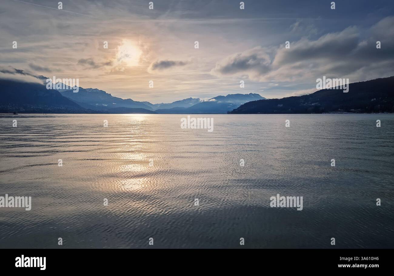 Serene glacier lake of Annecy with gentle ripples on the water's surface, reflecting the soft light of the setting sun. Aravis mountains range in the - Smartphone Captured Stock Image