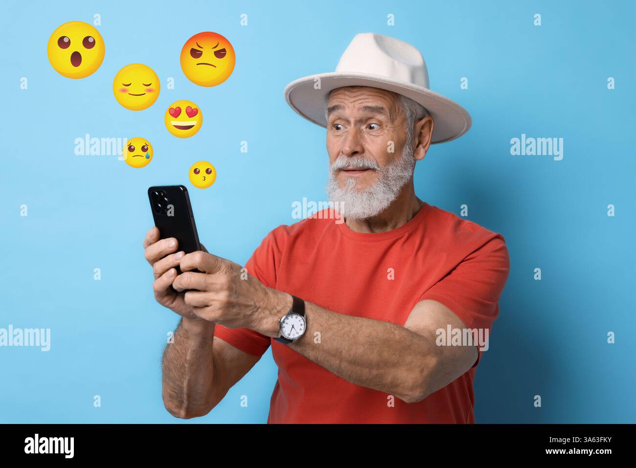 Social media. Surprised senior man using mobile phone on light blue background. Different emojis near gadget Stock Photo