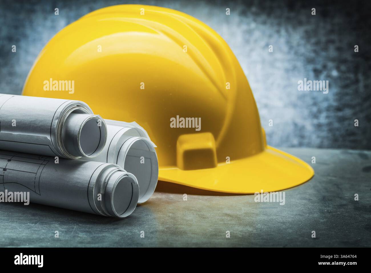 Rolls of blueprints and yellow construction helmet on metalic ...